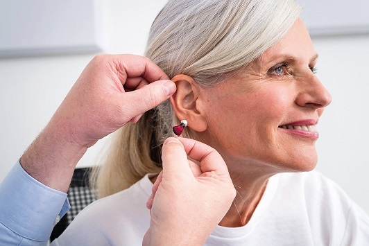 Seniorin bekommt ein modernes Hörgerät eingesetzt, Hörakustiker berät zur Hörhilfe.